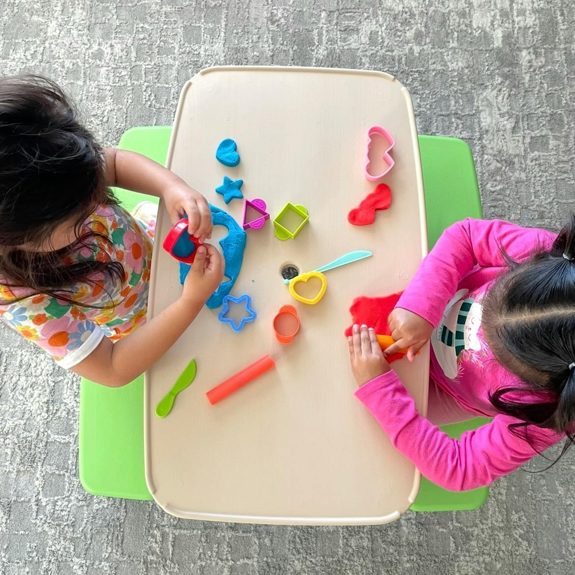 Two children playing with colorful playdough and cutters at a table