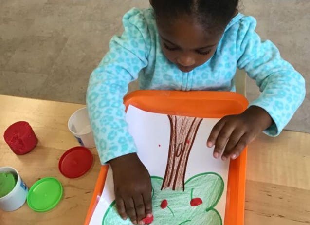 Child adding red dots to a drawing of a tree