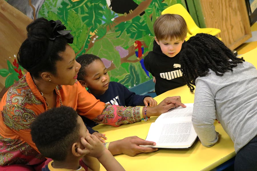 Adults and children gathered around a table with an open book
