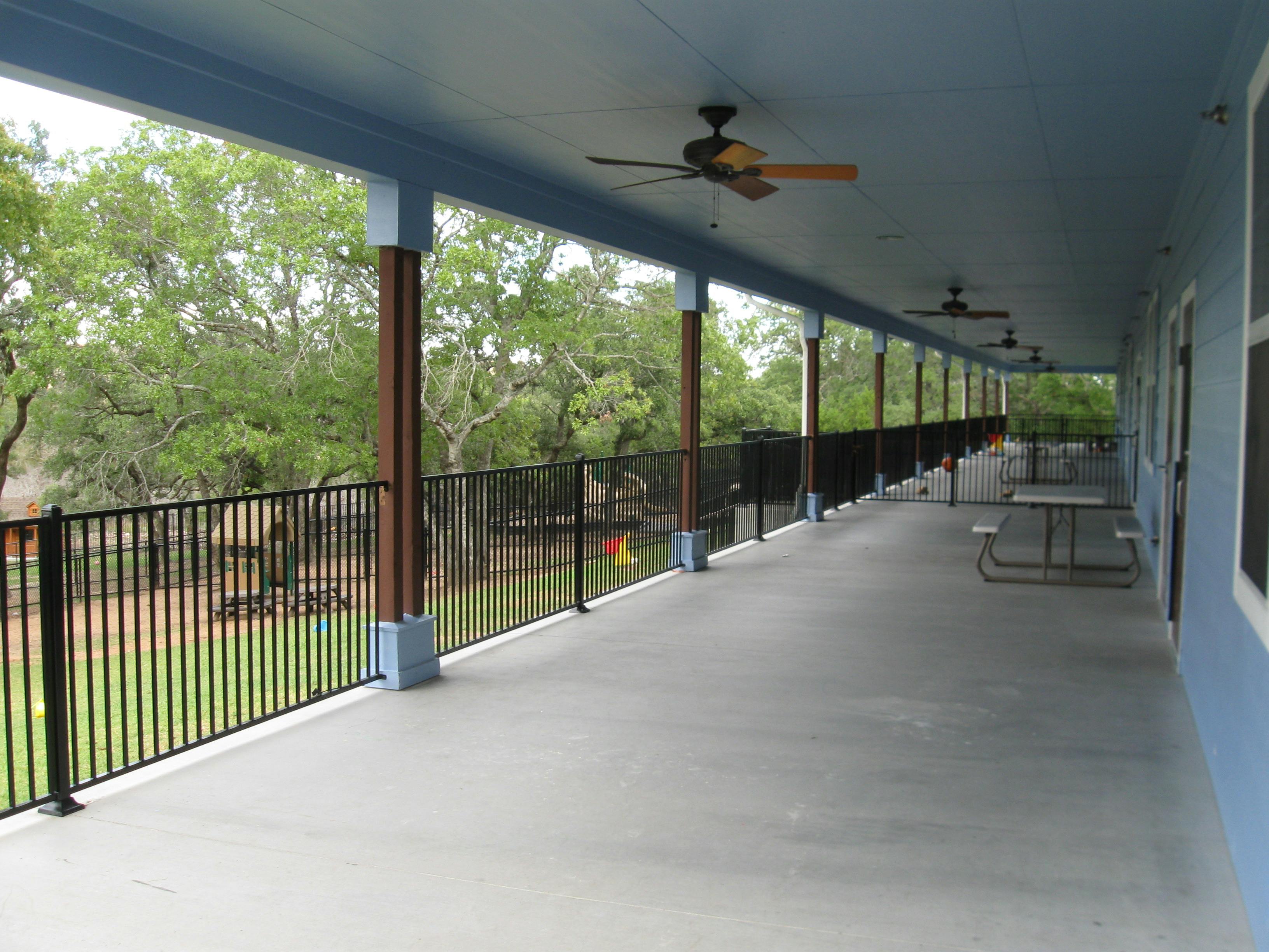 Long outdoor patio with ceiling fans and a black metal fence overlooking trees