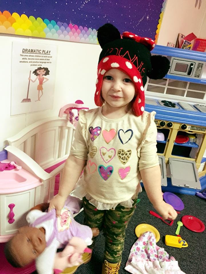 Child in a Minnie Mouse hat holding a doll in a play area
