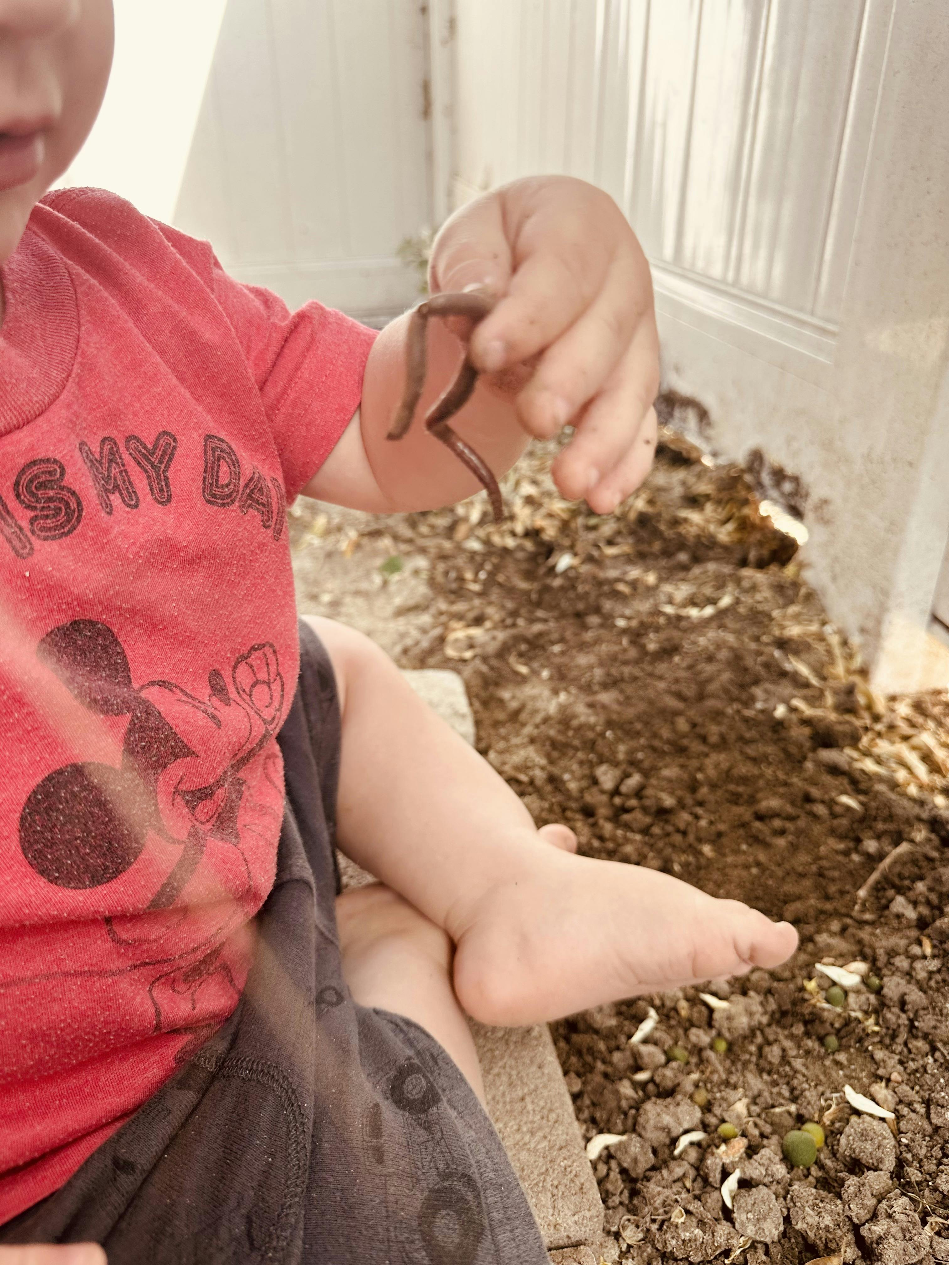 Child sitting on ground holding an earthworm