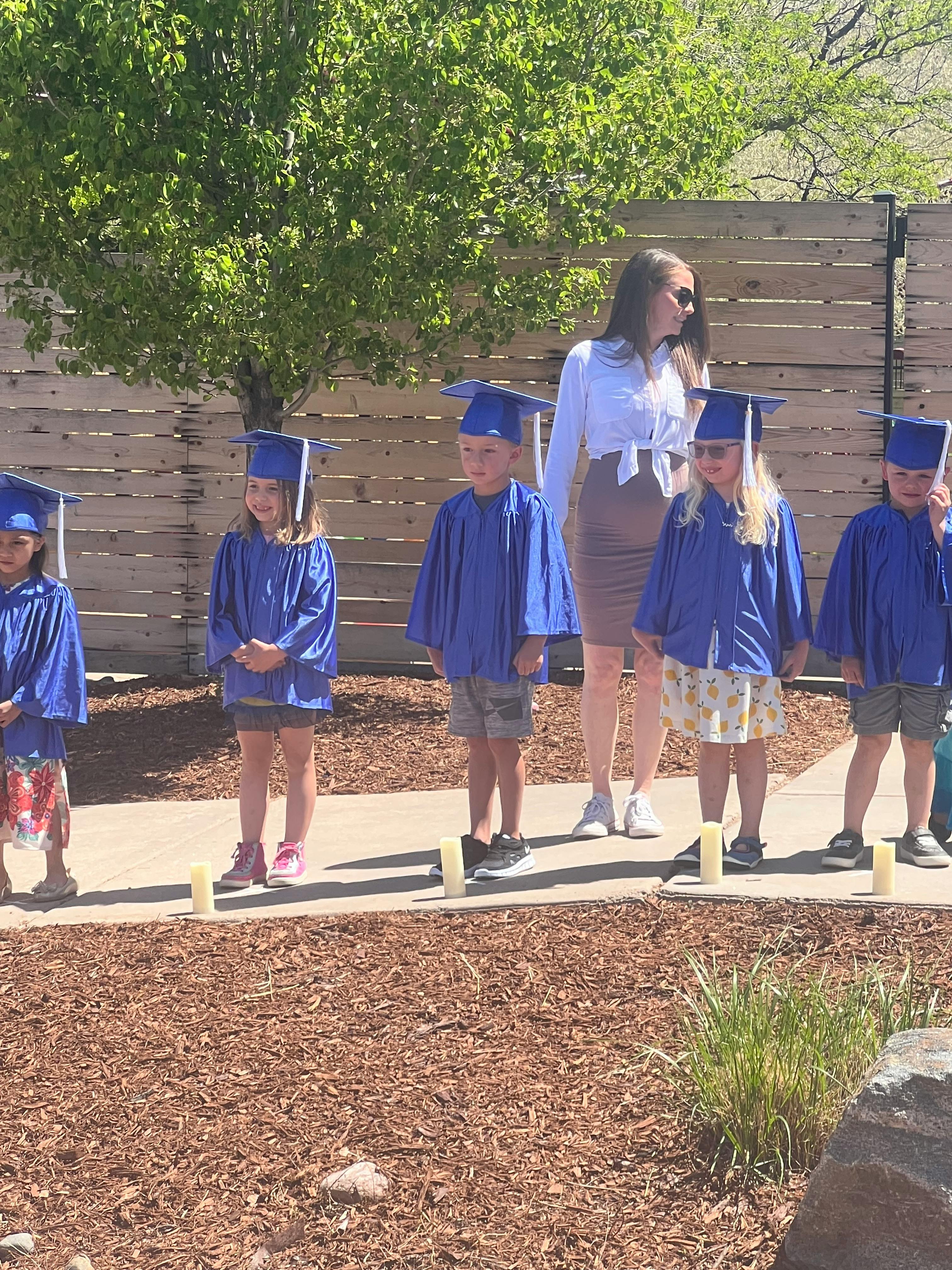Adult and children in graduation caps and gowns standing outdoors