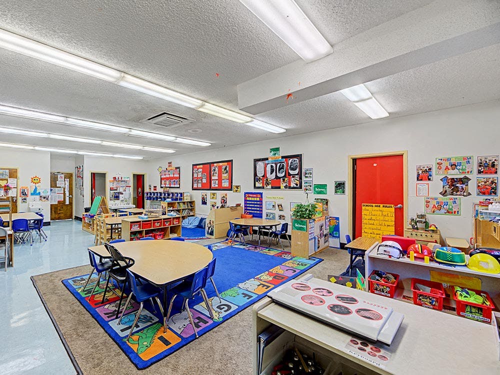 Classroom with small tables, chairs, and learning decorations on the walls