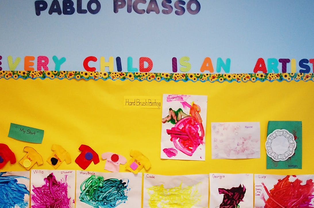 Children's artwork displayed on a yellow bulletin board with text "Every Child is an Artist"