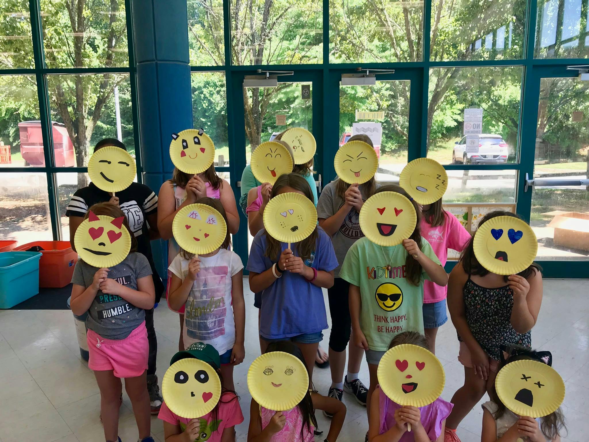 Group of children holding up paper plates with emoji faces drawn on them