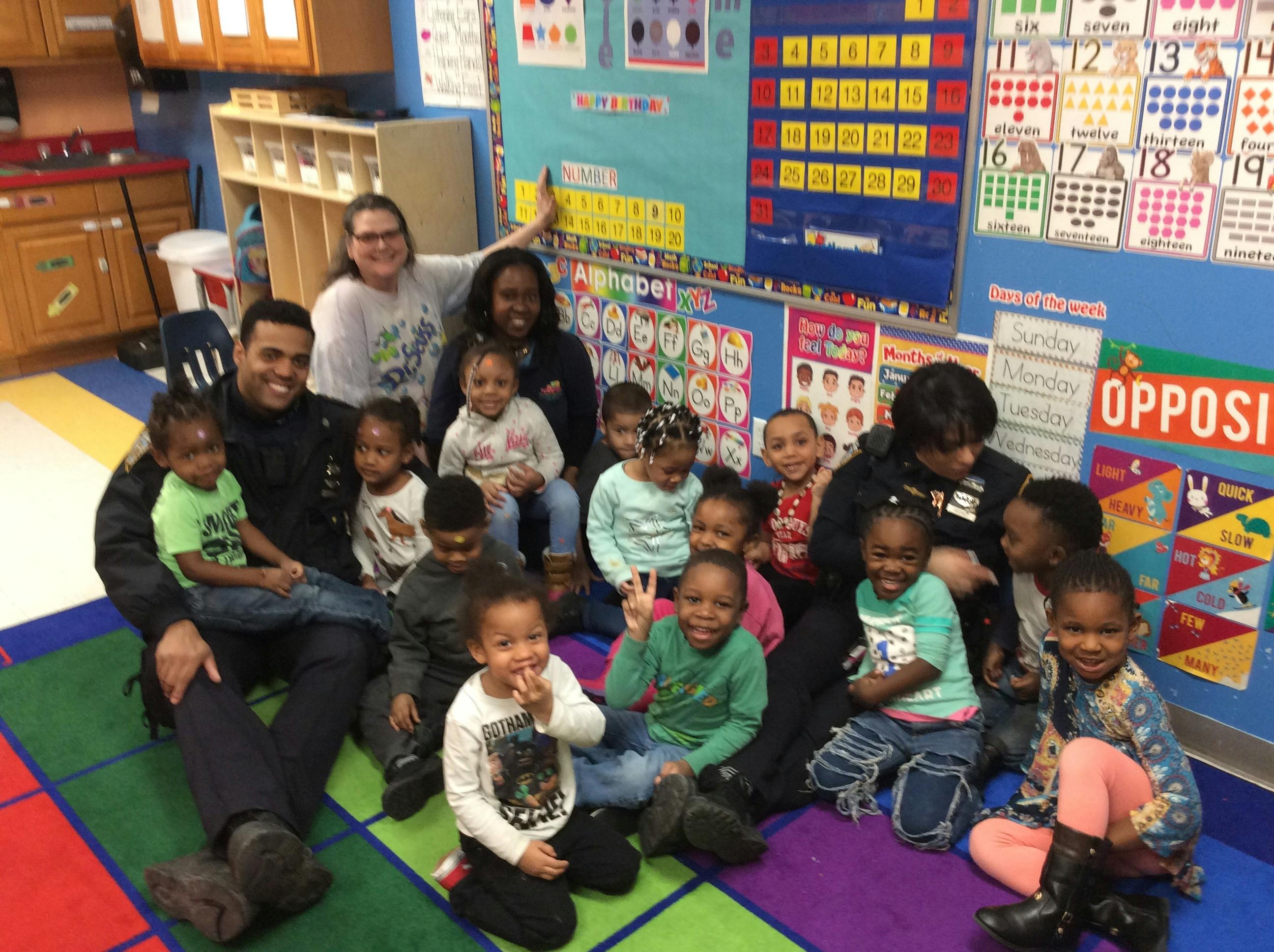 Adults and children sitting on a colorful rug in a classroom
