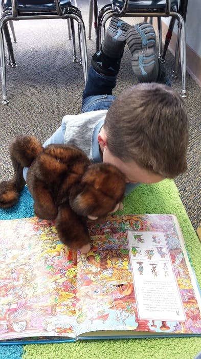 Child lying on floor reading a book with a stuffed animal