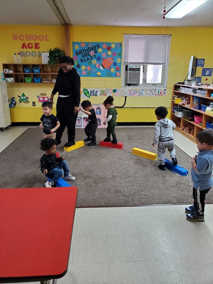 Adult and children playing with balance beams in a classroom