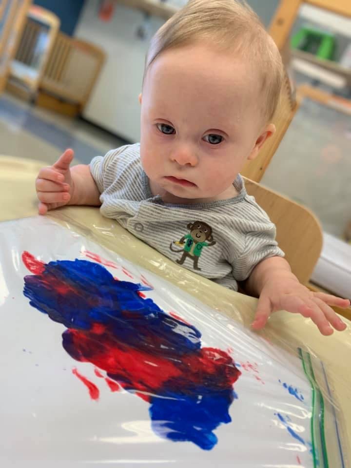 Child in a high chair with red and blue paint in a plastic bag
