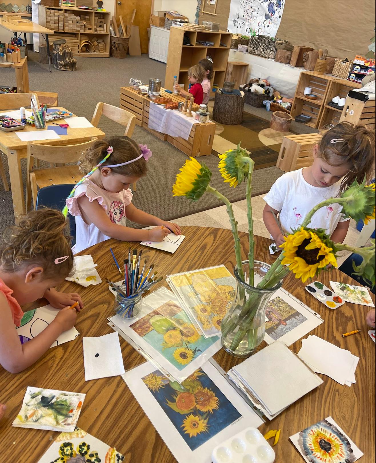 Children sitting at a table drawing and painting in a classroom