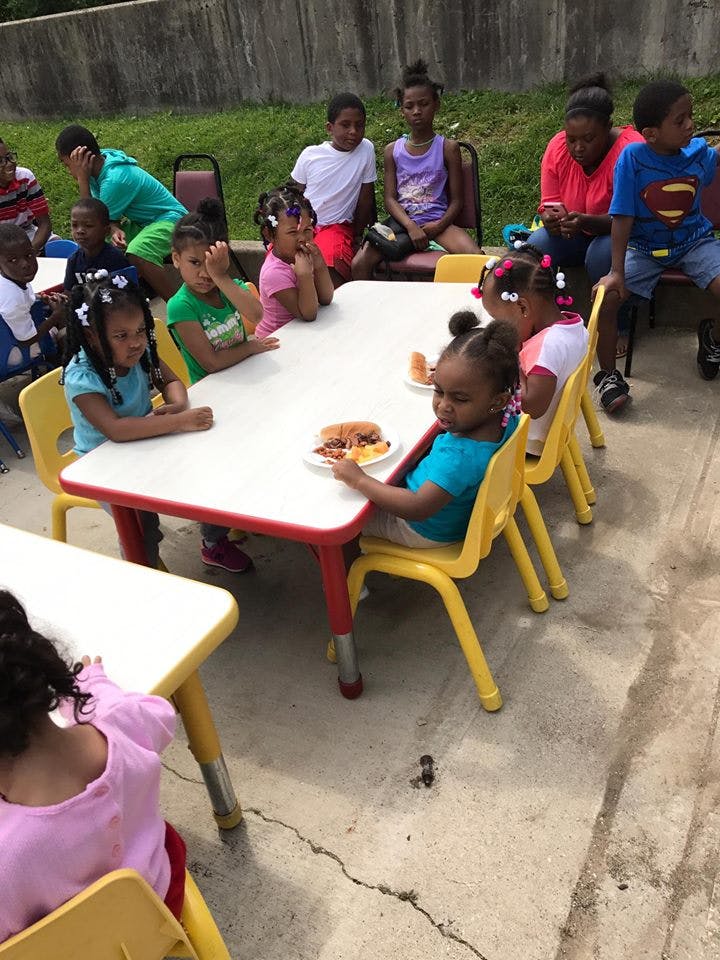 Children sitting at small tables outdoors, some eating