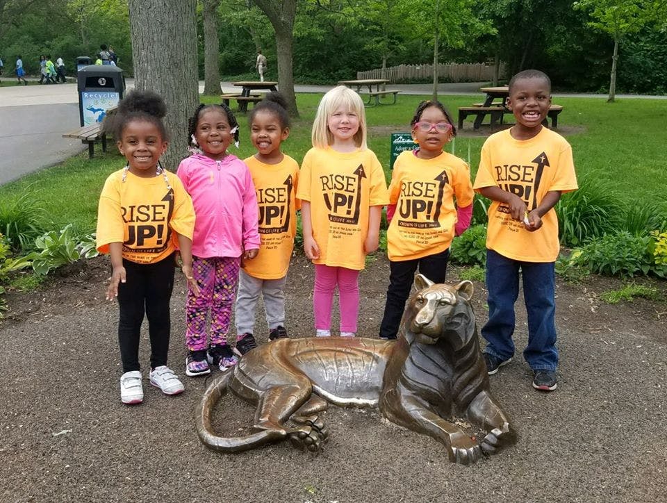 Six children standing around a bronze statue of a tiger