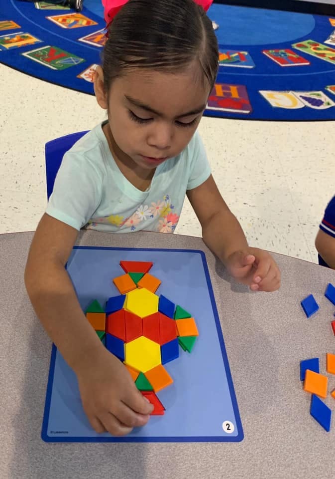 Child creating a design with colorful geometric shapes on a blue board