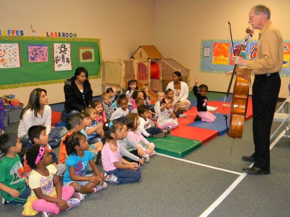 Adult playing cello for children and adults in a classroom
