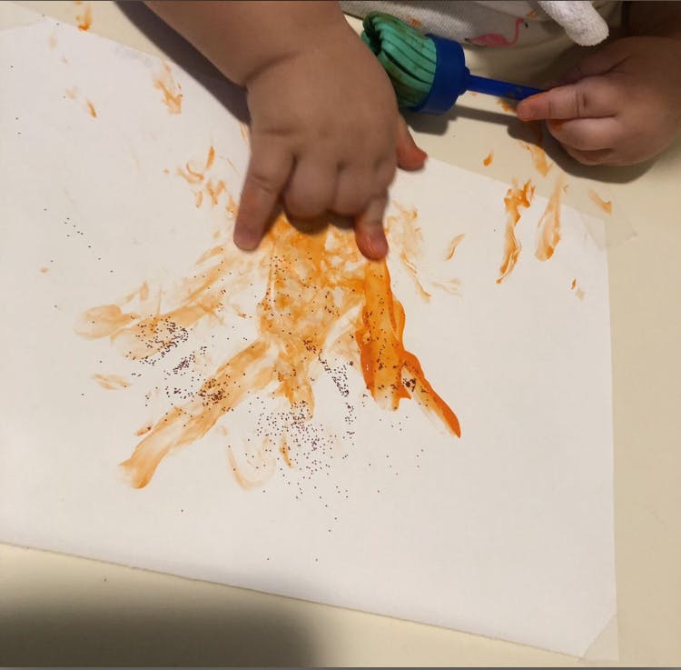 Child's hands painting with orange paint and a brush