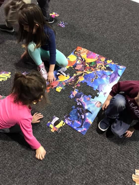 Children on a carpet assembling a large colorful floor puzzle