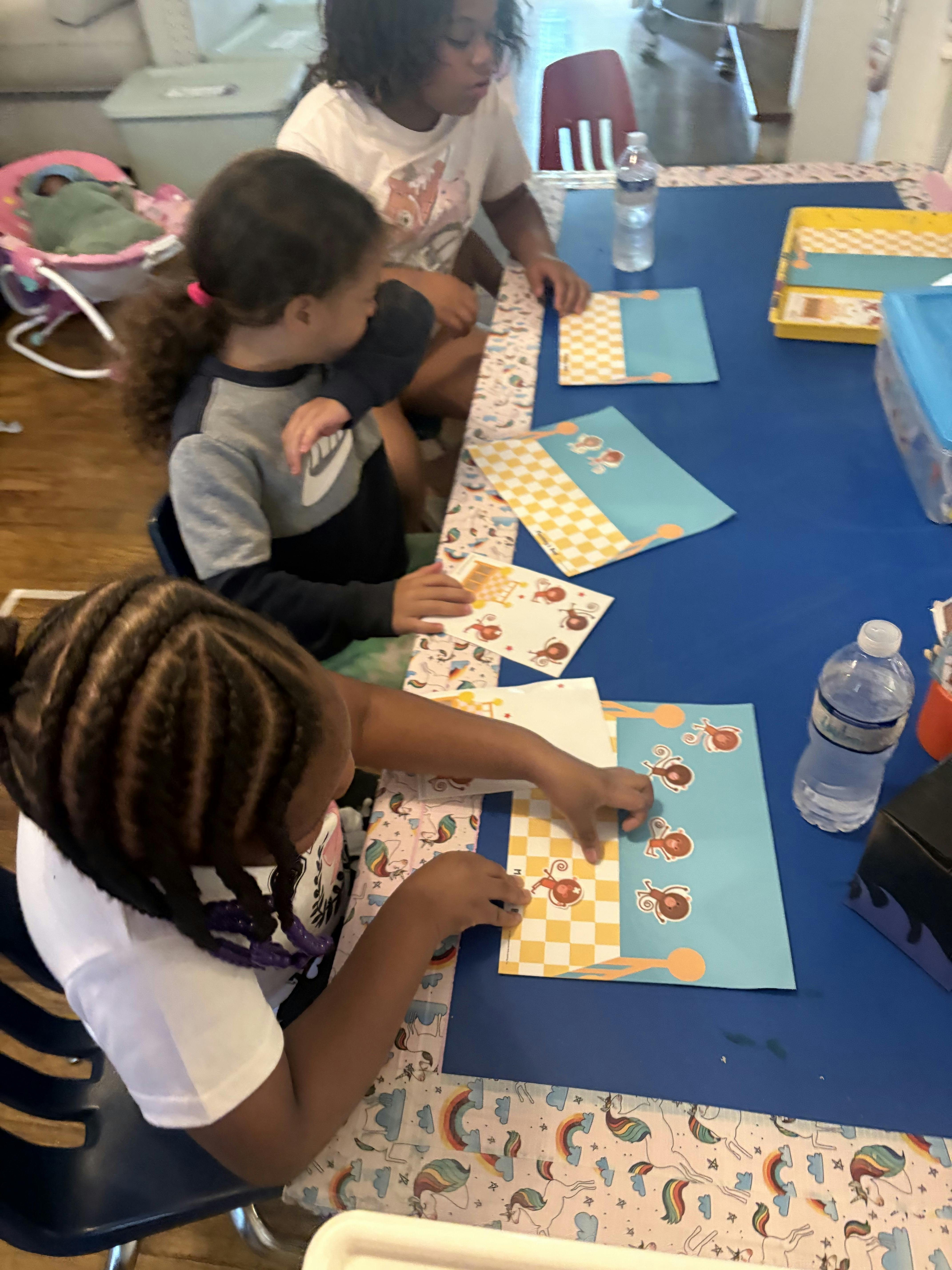 Three children working on craft projects at a blue table