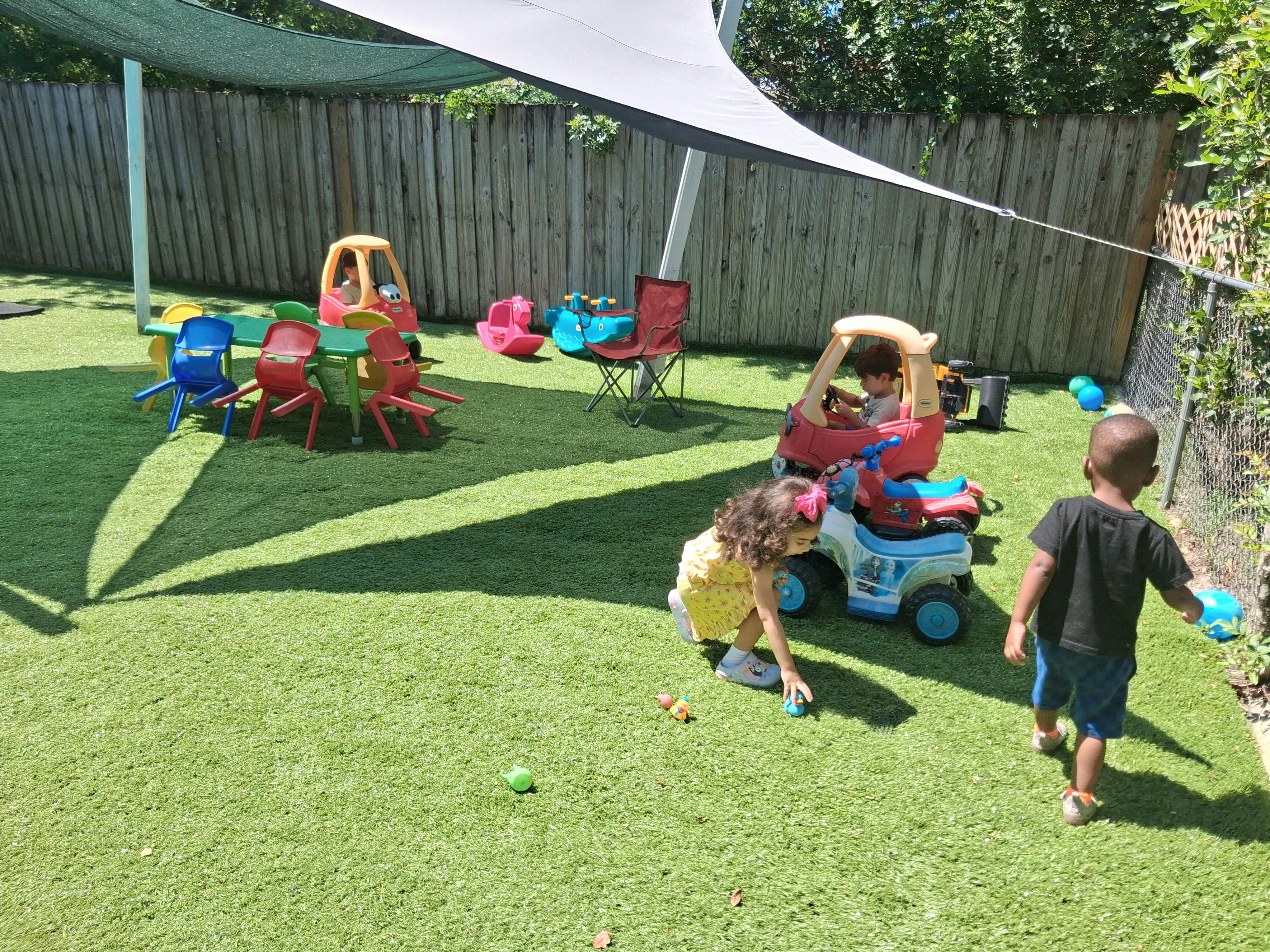 Children playing with toy cars and small furniture in a fenced backyard