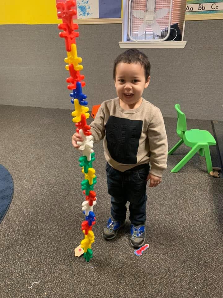 Child standing next to a tall stack of colorful interlocking toys