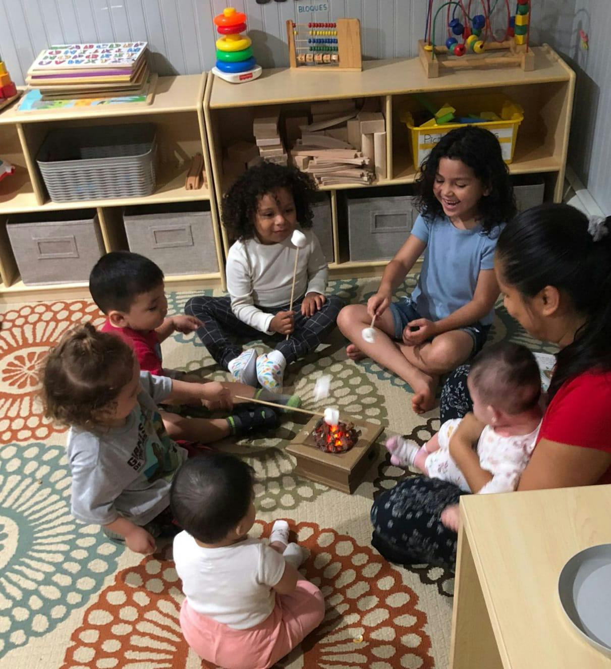 People and children sitting on a rug around a pretend campfire with marshmallows