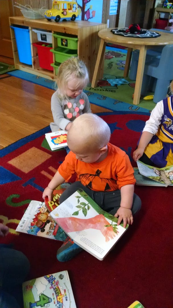 Three children sitting on a rug looking at books