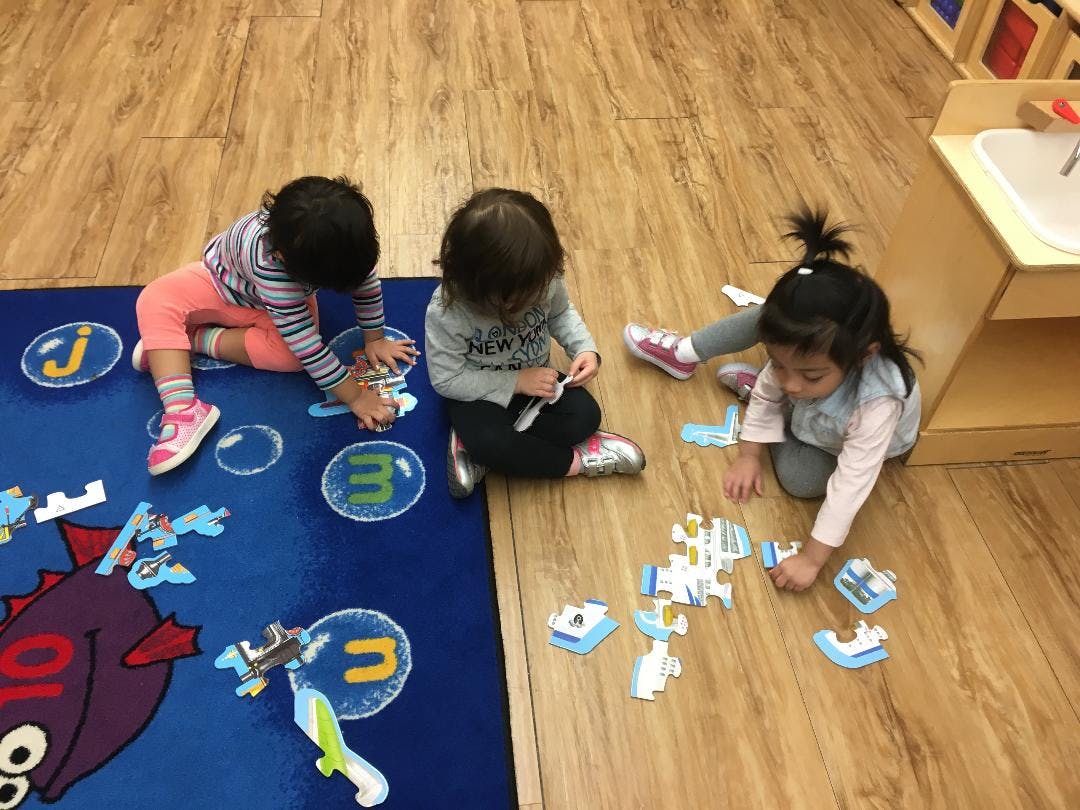 Three children playing with puzzles on a rug and wooden floor
