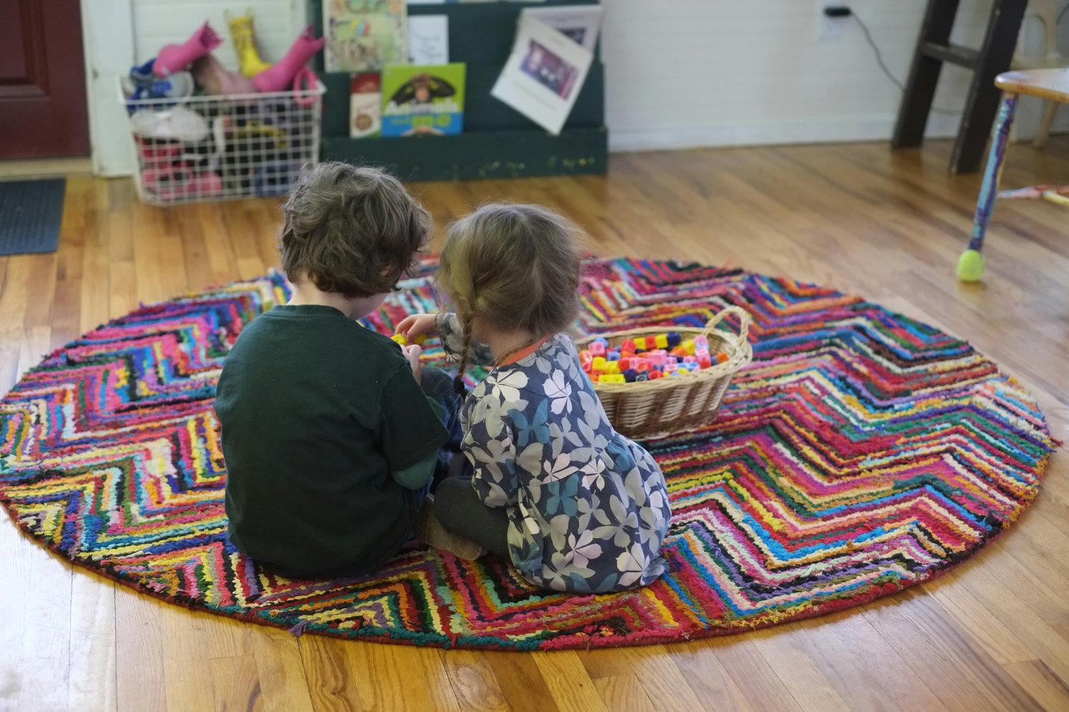 Two children sitting on a colorful rug playing with blocks