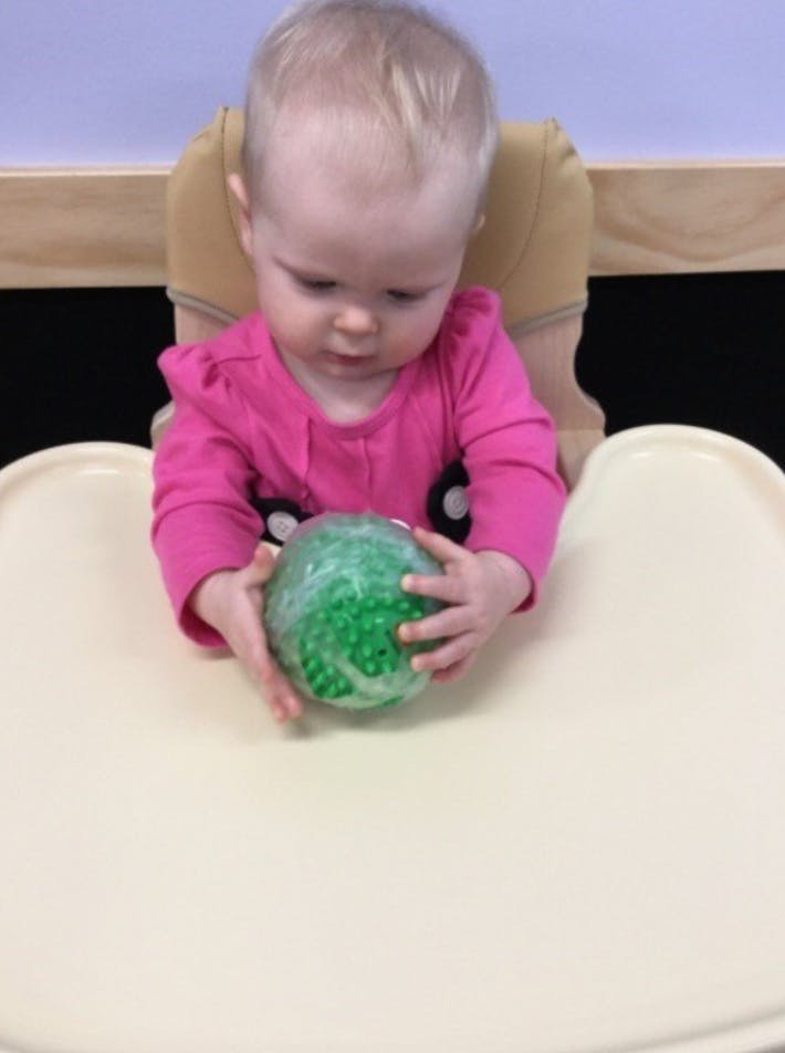 Child in a high chair holding a green ball