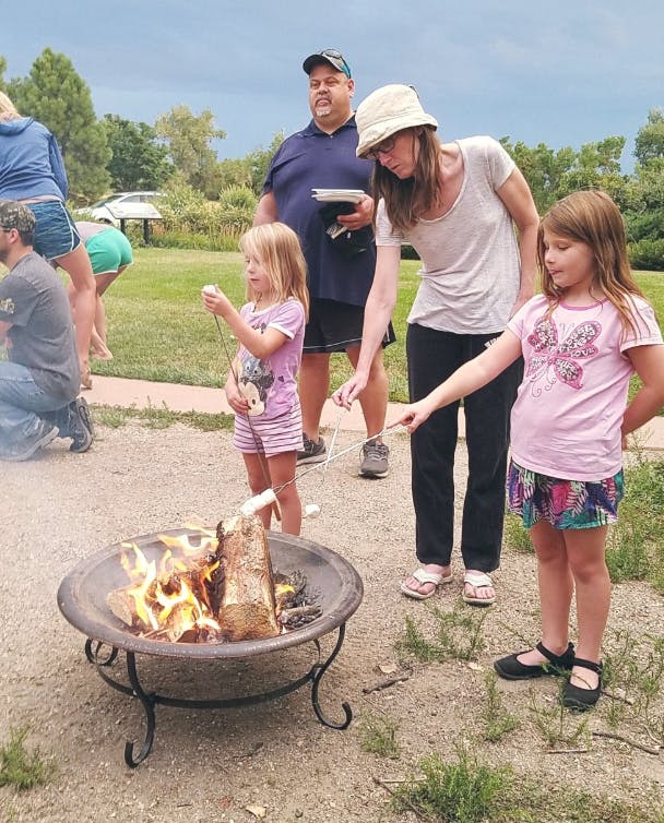 People and children roasting marshmallows over a fire pit