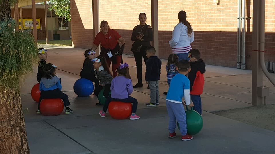 Children sitting on and holding exercise balls with adults nearby