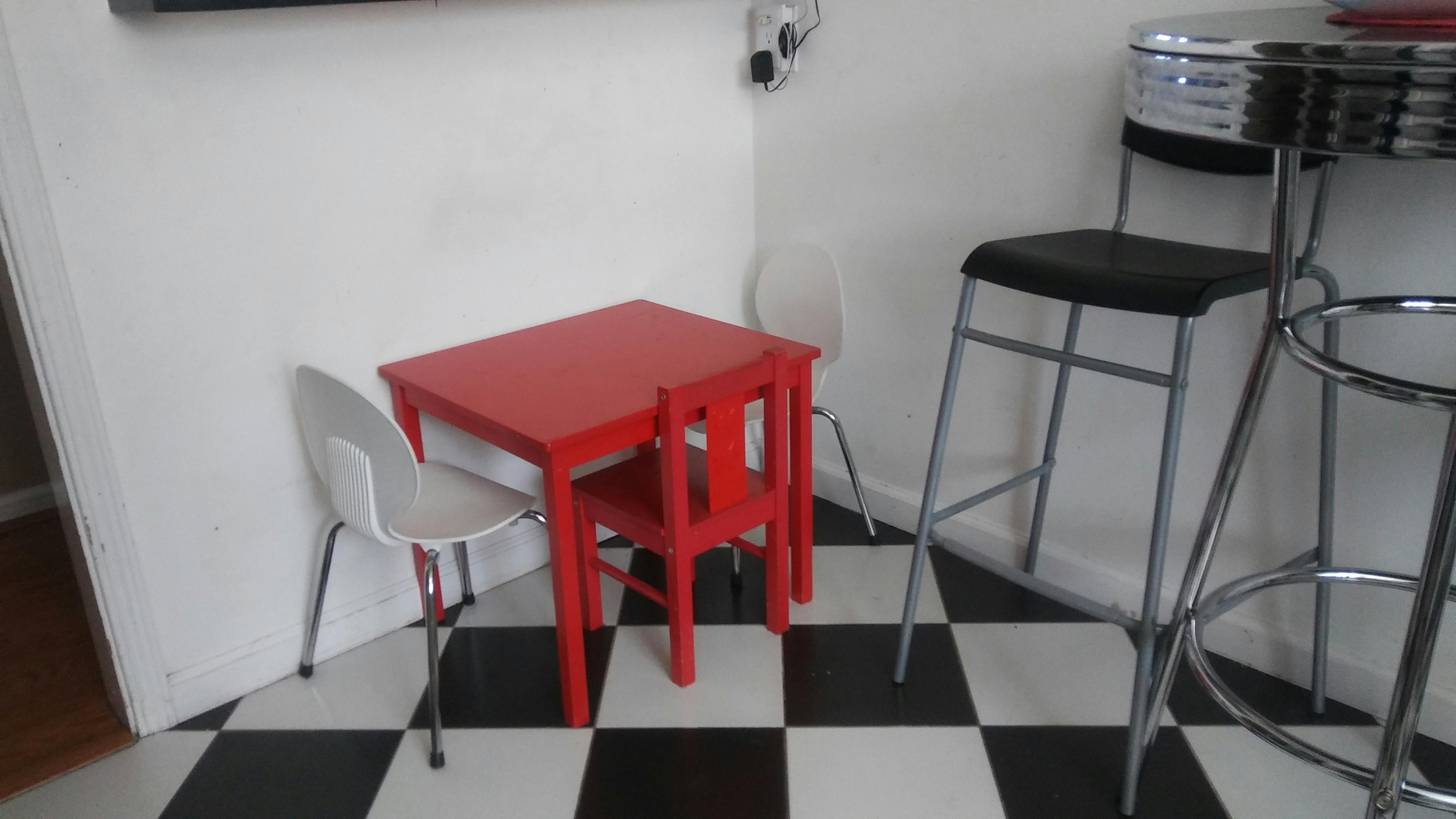 Red child's table and chair next to bar stools on a checkered floor