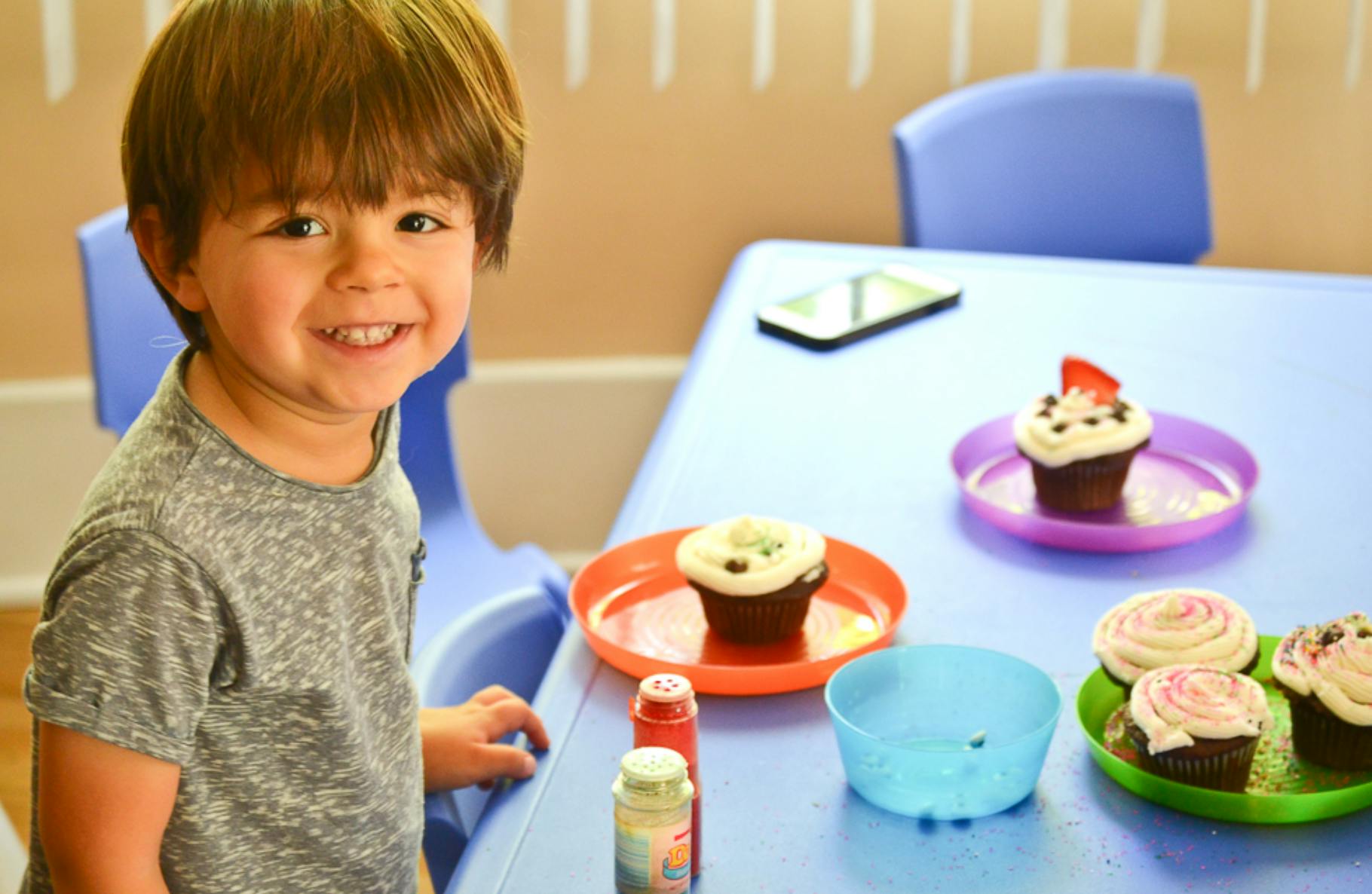 Child smiling at a table with cupcakes and decorating supplies