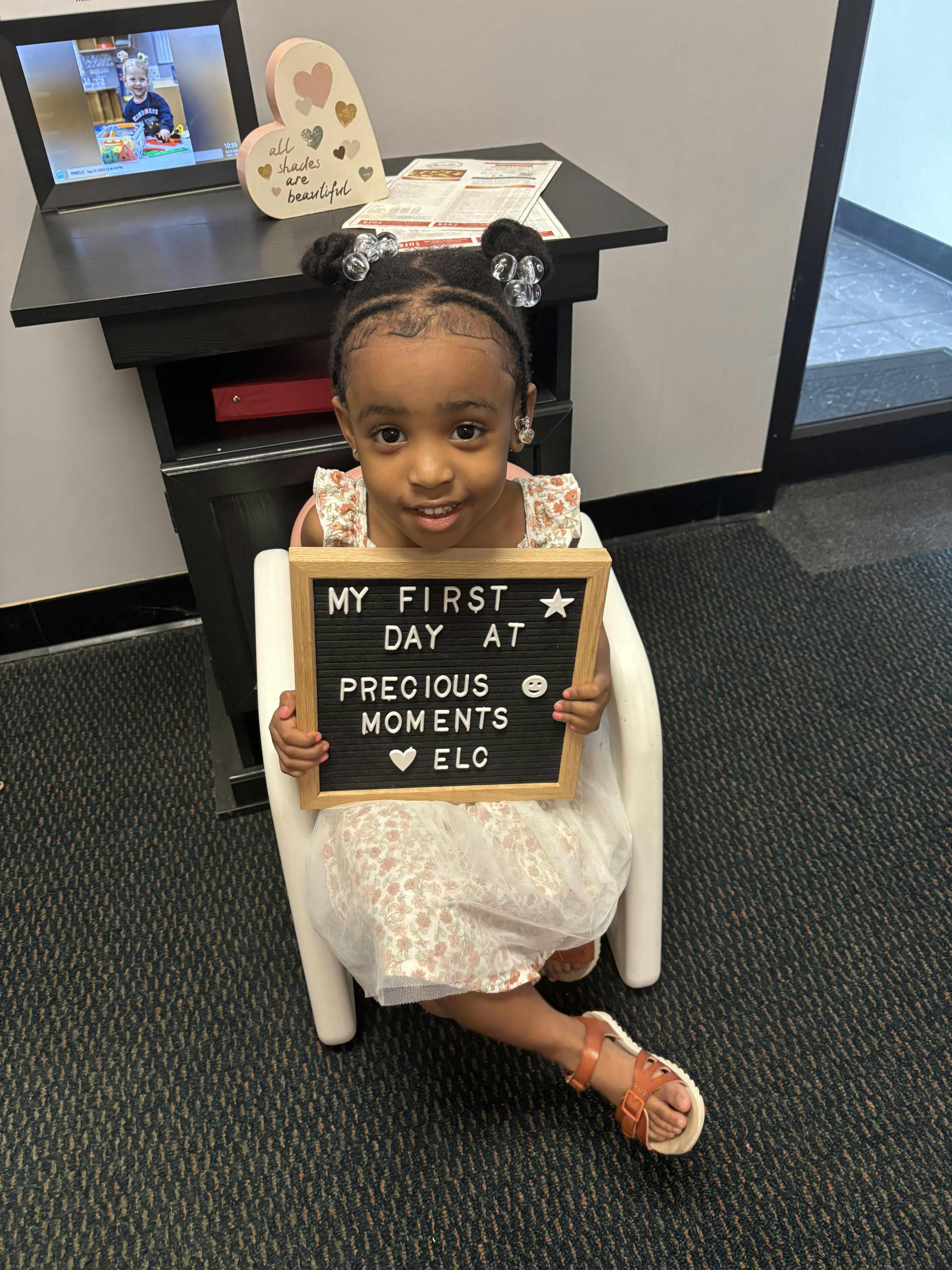 Child holding a sign that reads "MY FIRST DAY AT PRECIOUS MOMENTS ELO"