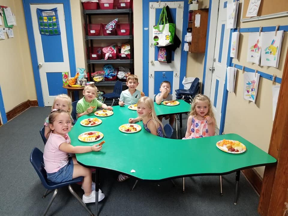 Children sitting at tables with plates of food in a classroom
