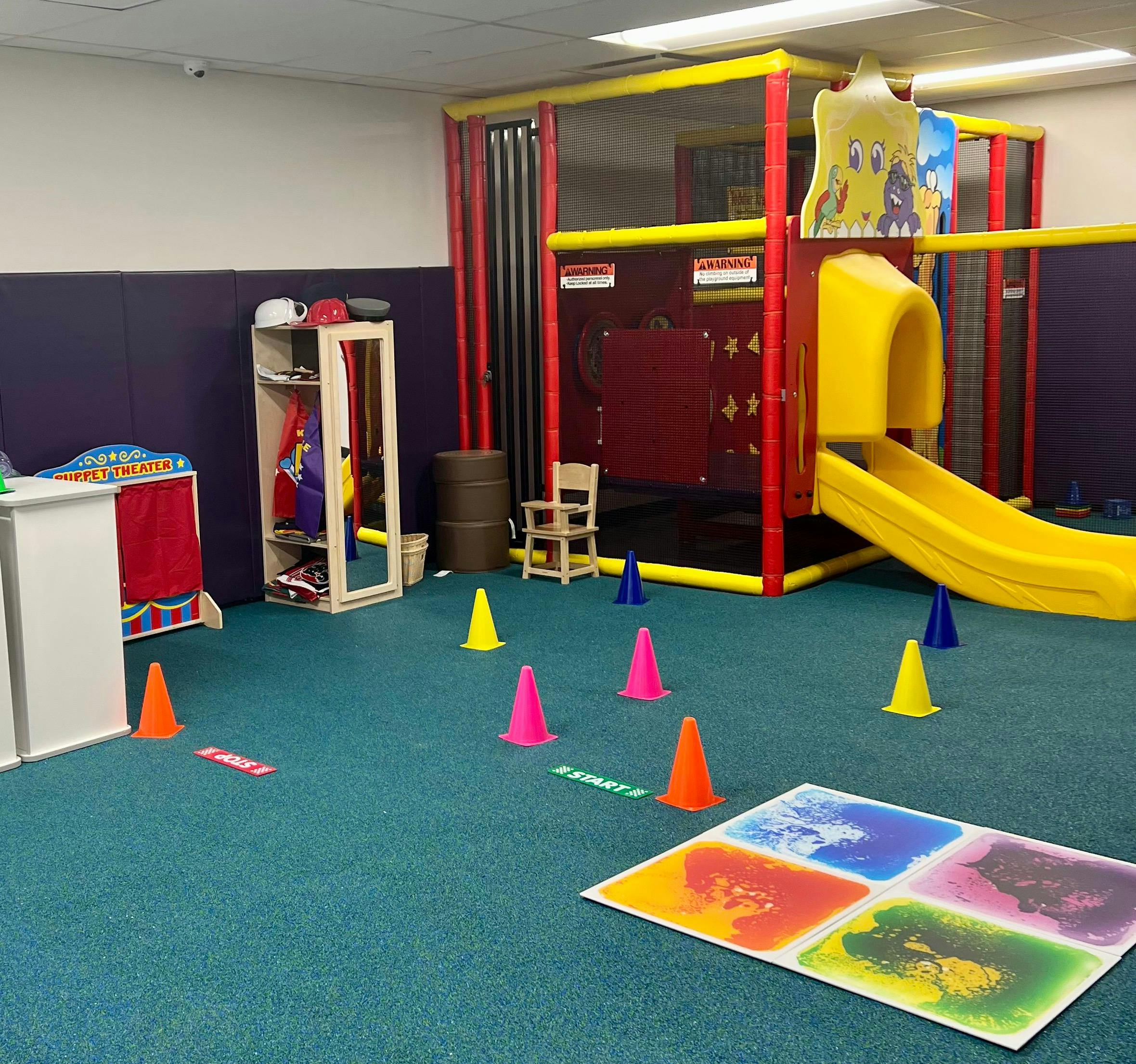 Indoor playground with a yellow slide, play structure, and colorful cones on the floor