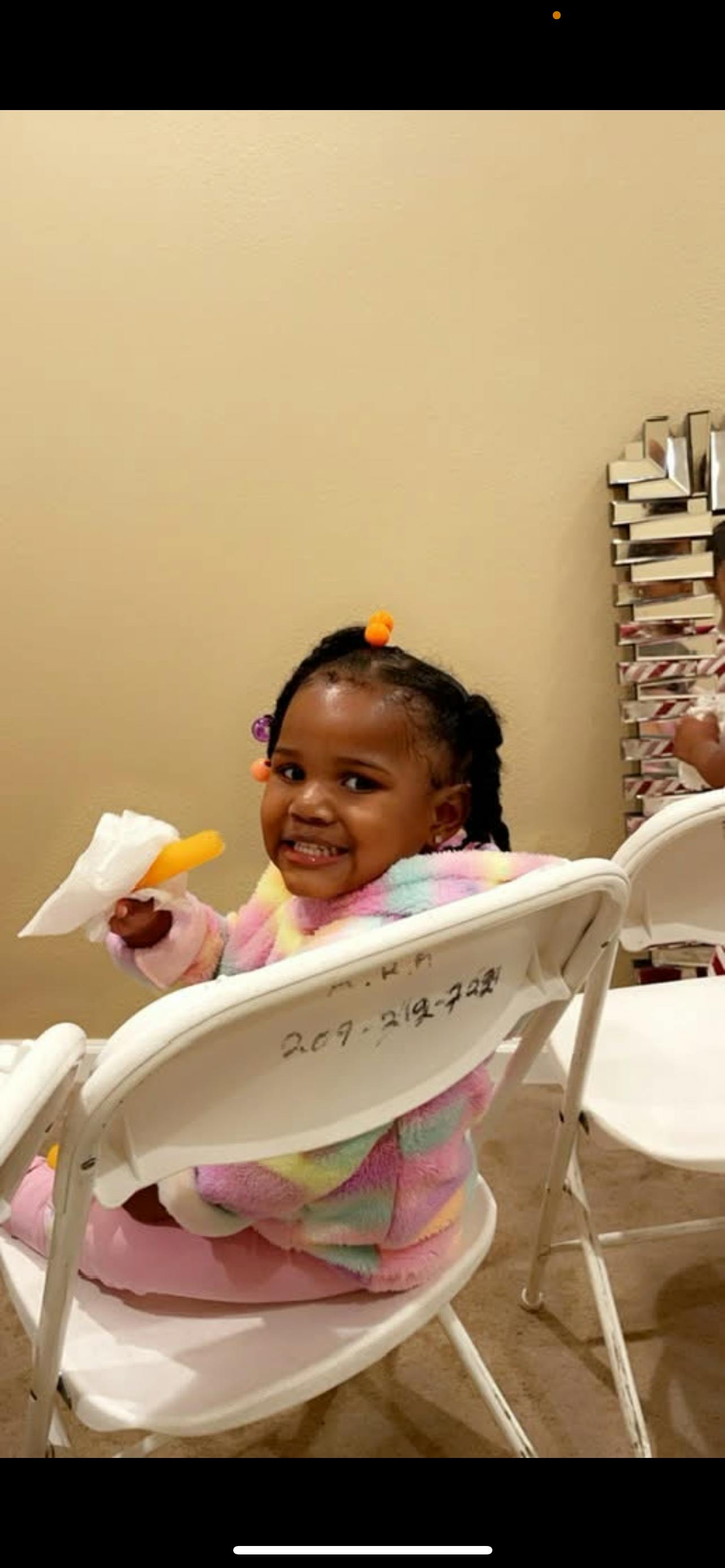 Child sitting in a white chair holding a snack