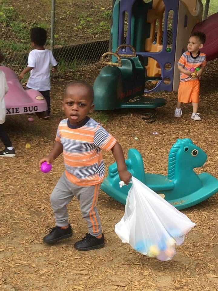 Child holding a purple ball and a bag of colorful balls on a playground