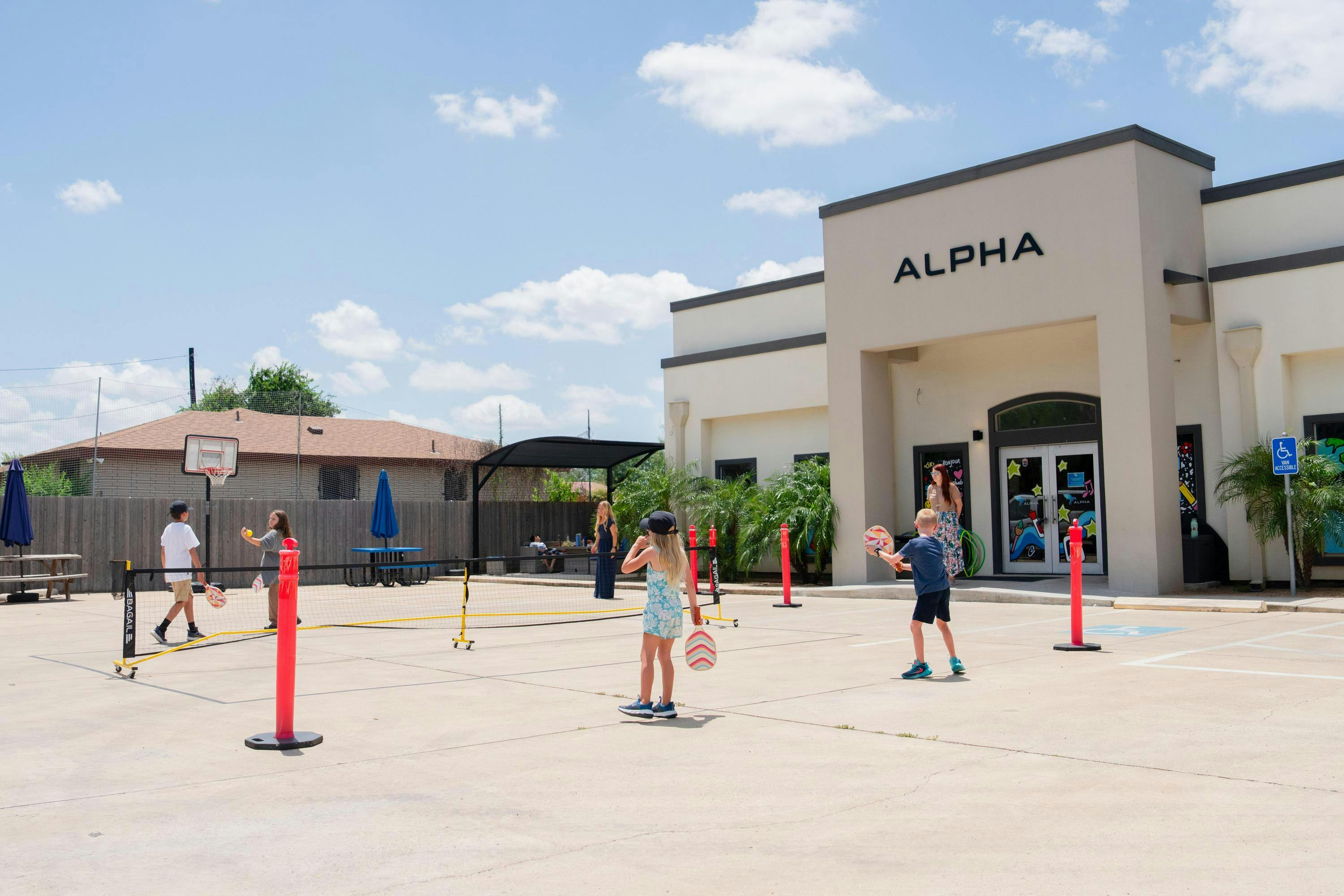 Children playing pickleball on an outdoor court next to a building