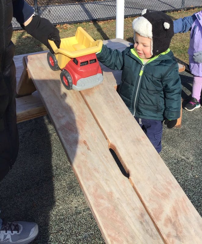 Child and person playing with a toy truck on a wooden ramp