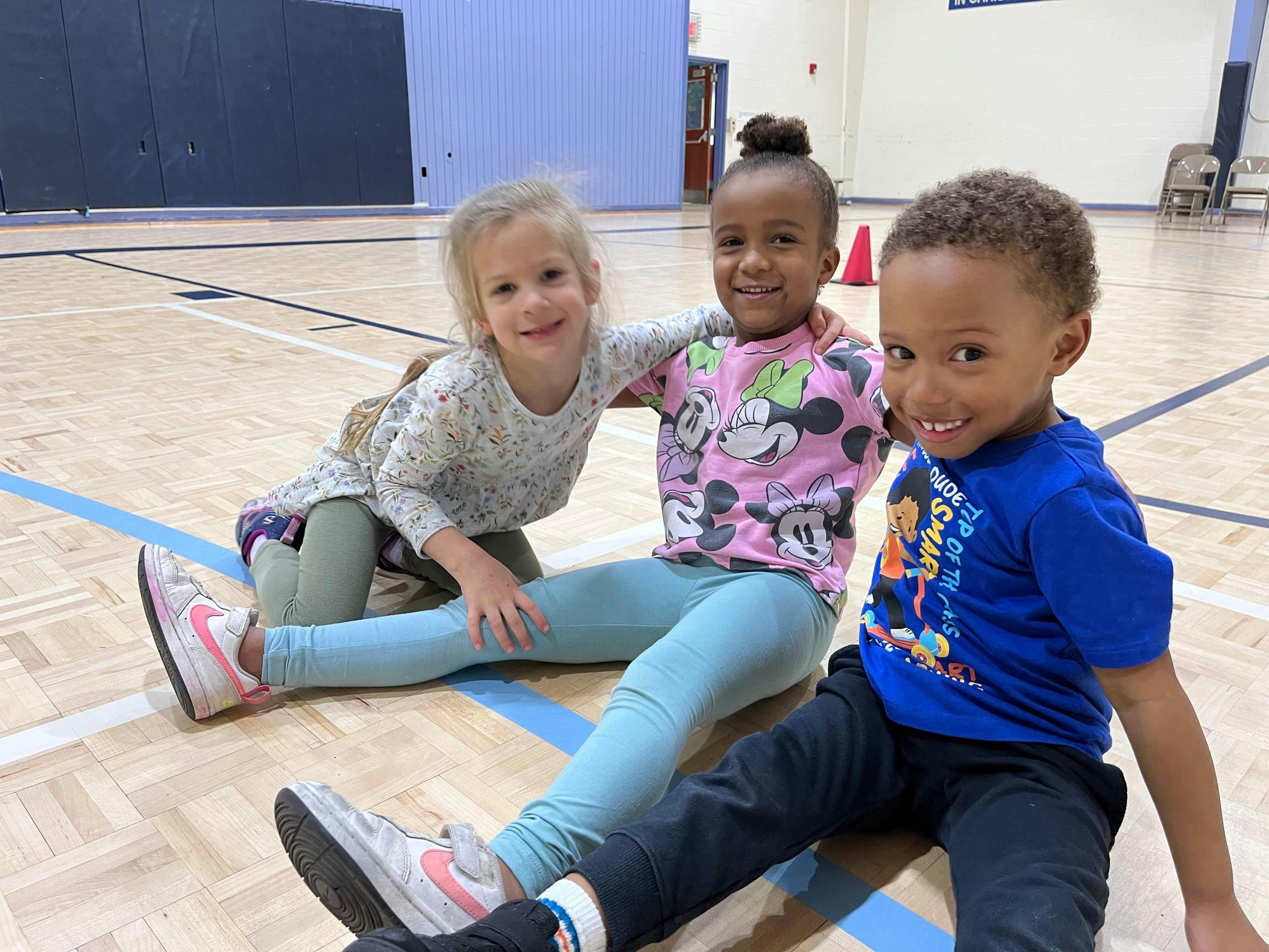 Three children sitting on a gym floor