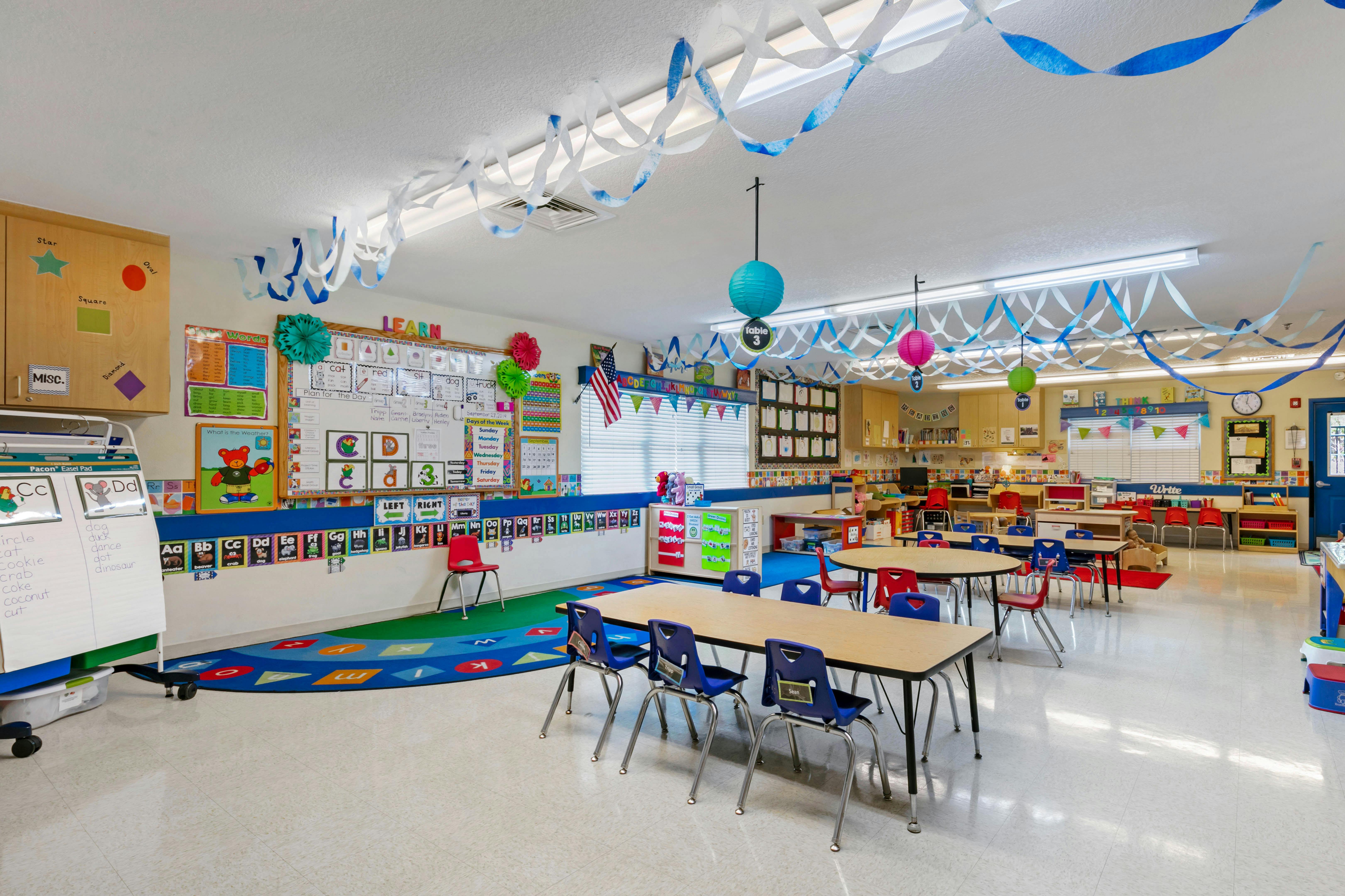 An empty early childhood classroom with colorful decorations and small tables and chairs