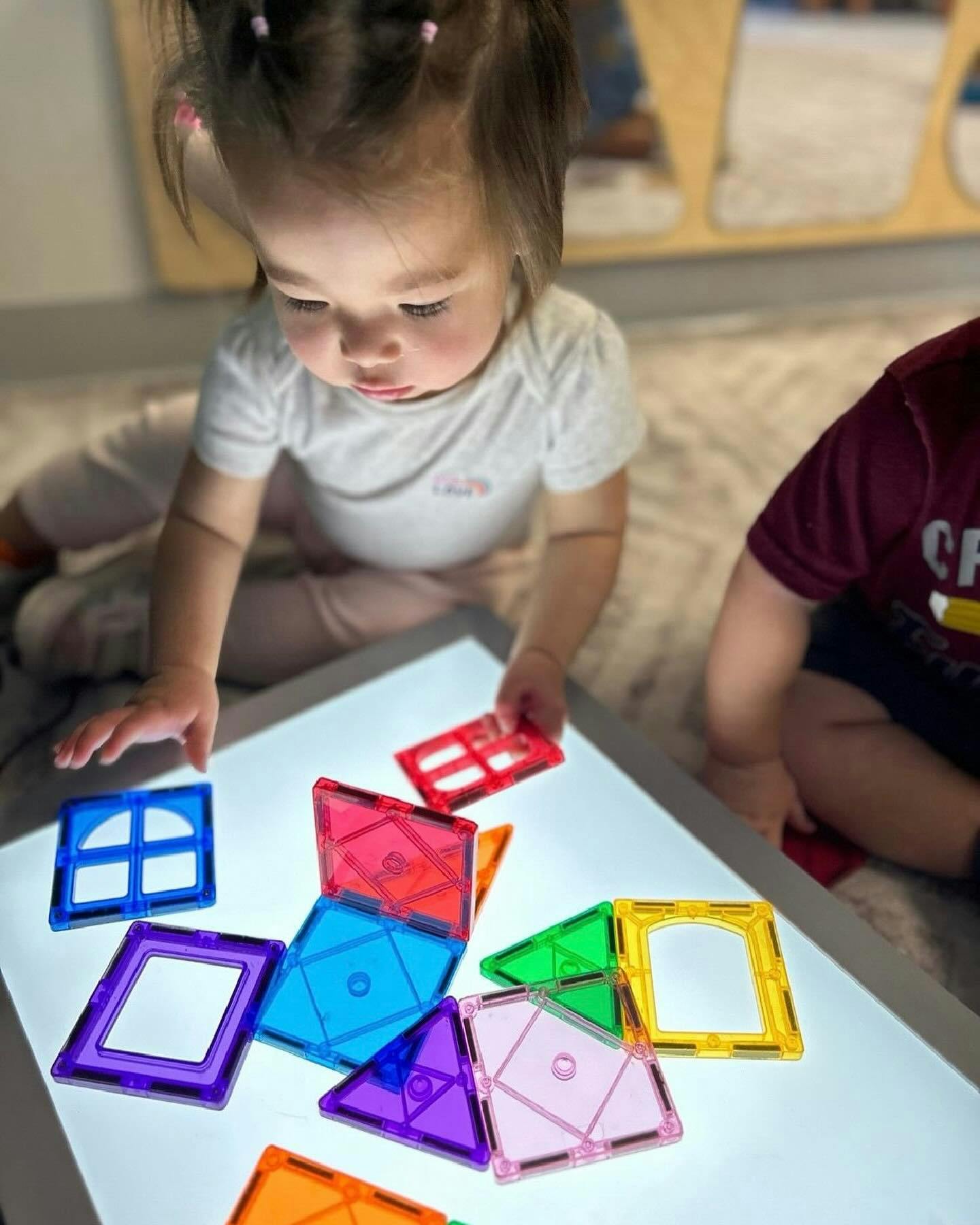 Child playing with colorful magnetic tiles on a light table