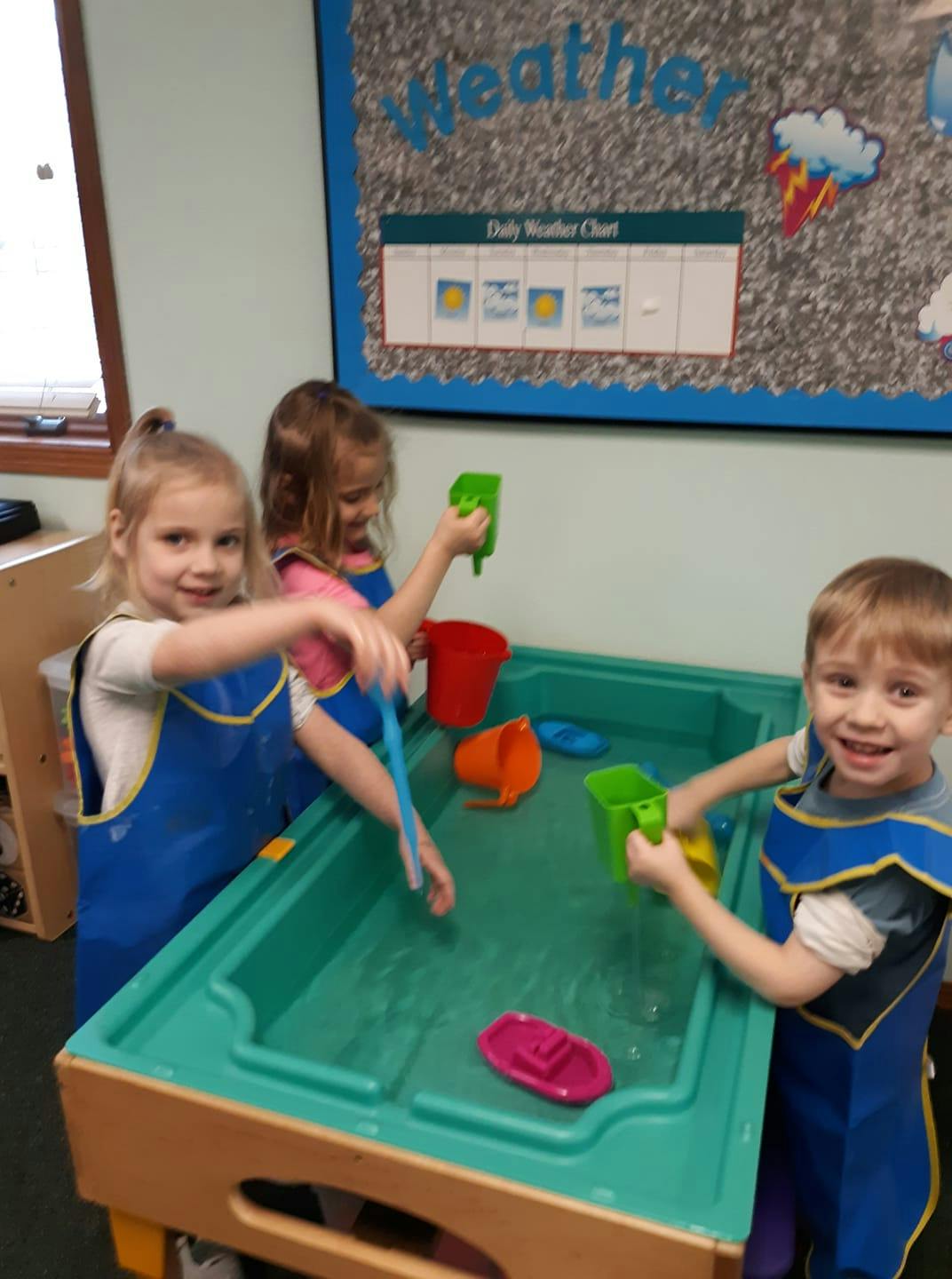 Three children playing with water and toys at a water table