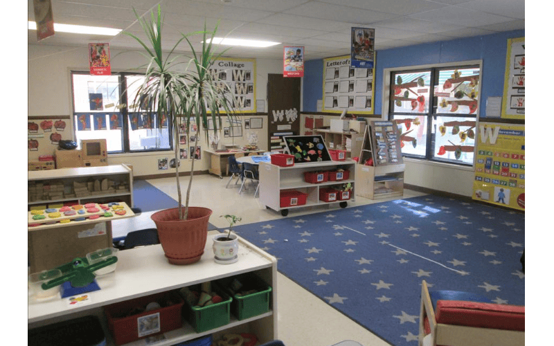 A classroom with activity centers, a blue rug with white stars, and windows with art