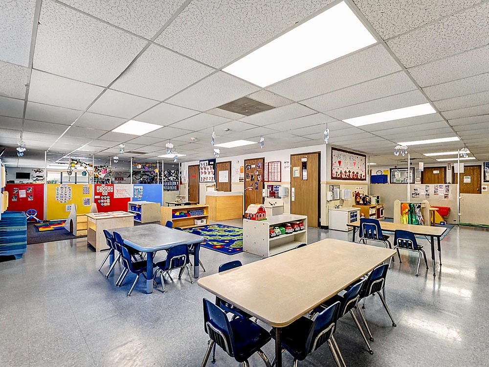Empty classroom with small tables and chairs, colorful dividers, and play areas