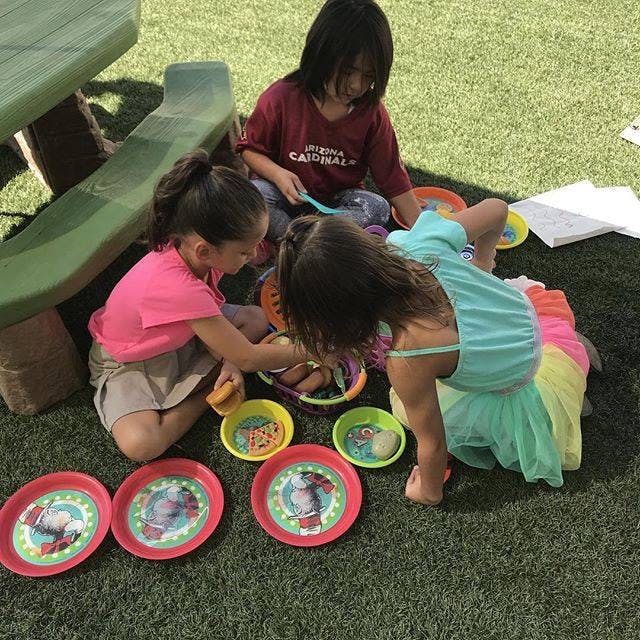 Three children playing with plates and bowls on artificial grass