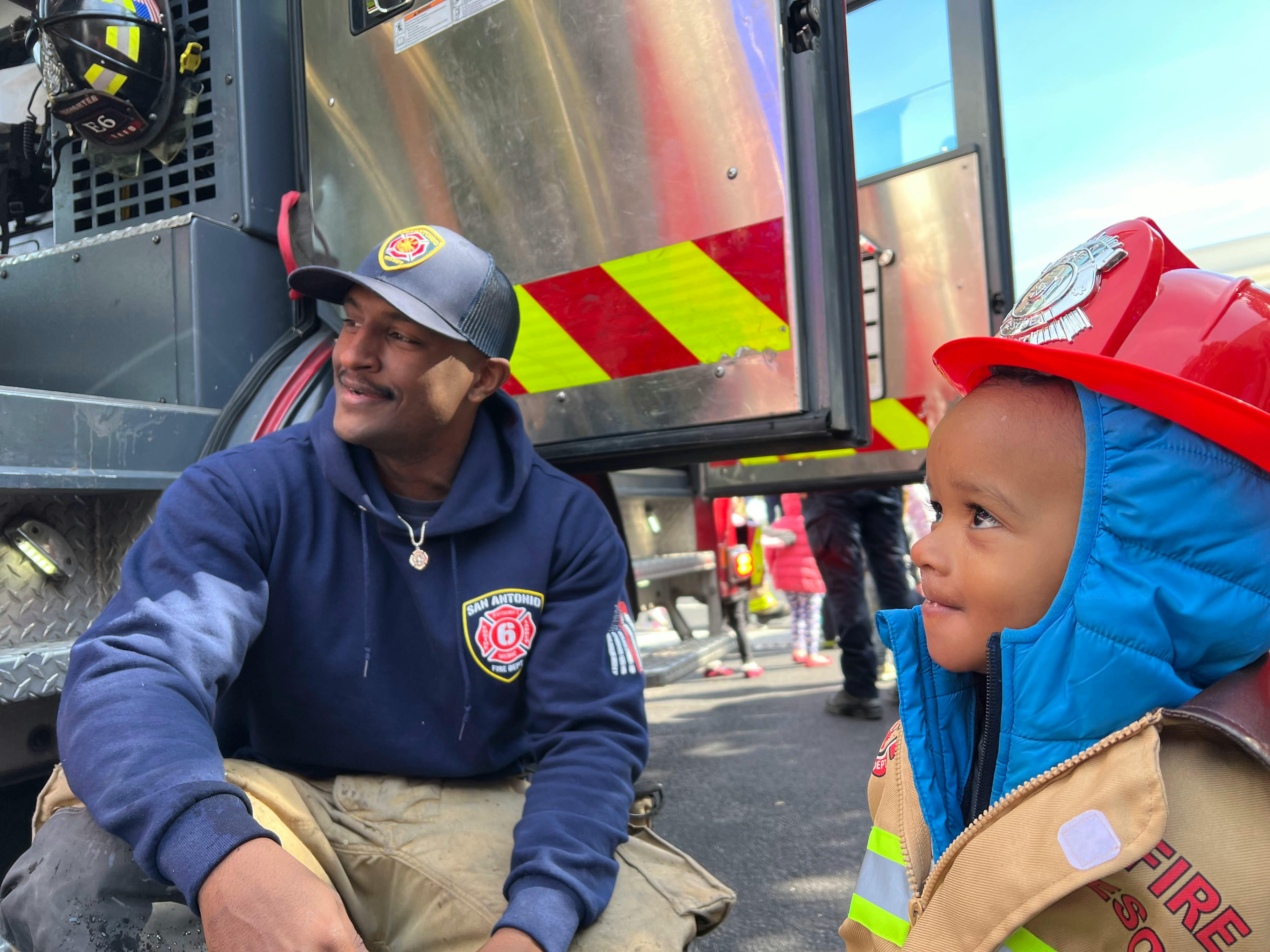Person in uniform and child in firefighter costume next to a fire truck
