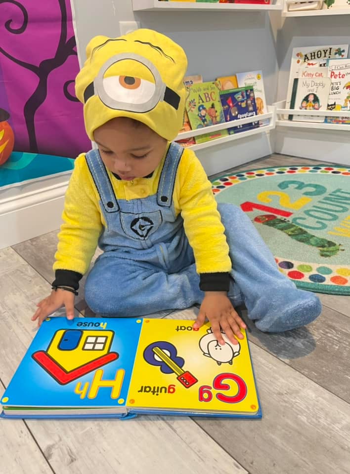 Child in a yellow costume sitting on the floor looking at an open book