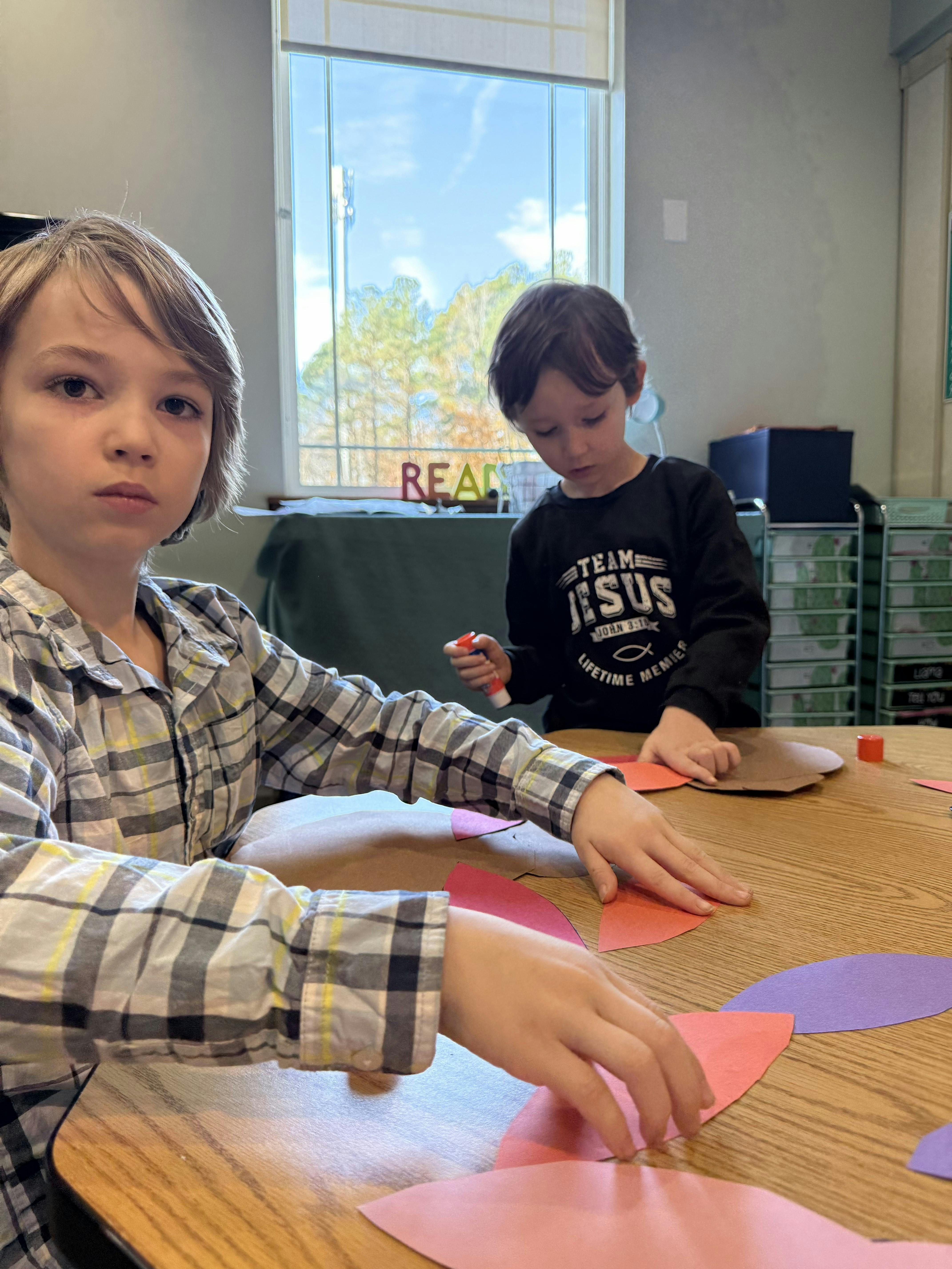 Two children making crafts at a table with colorful paper cutouts